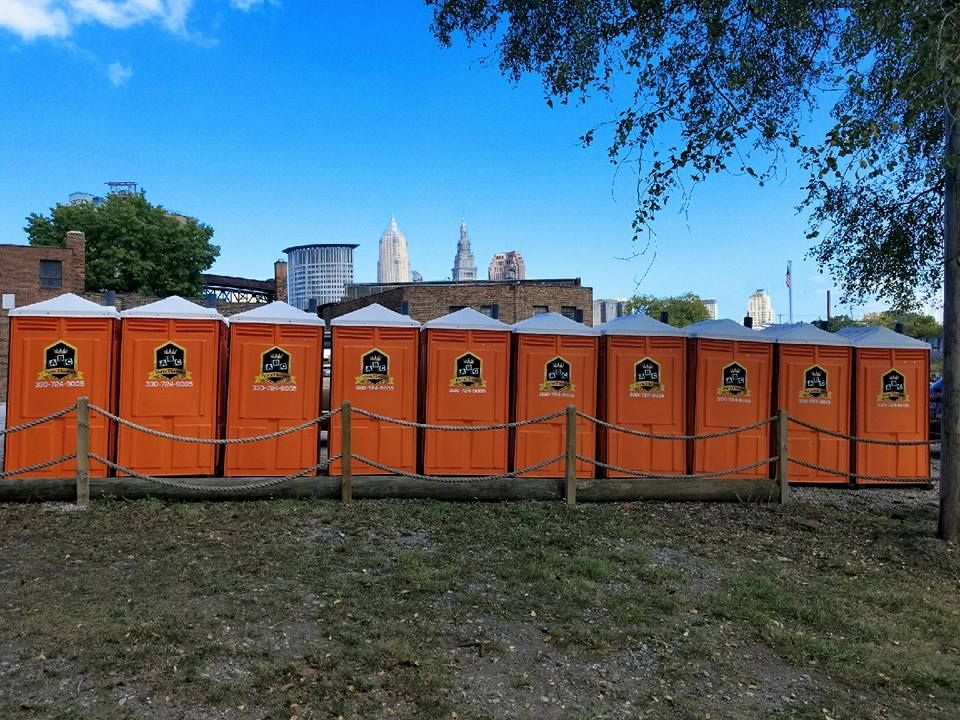 A row of orange portable toilets are lined up in a field.