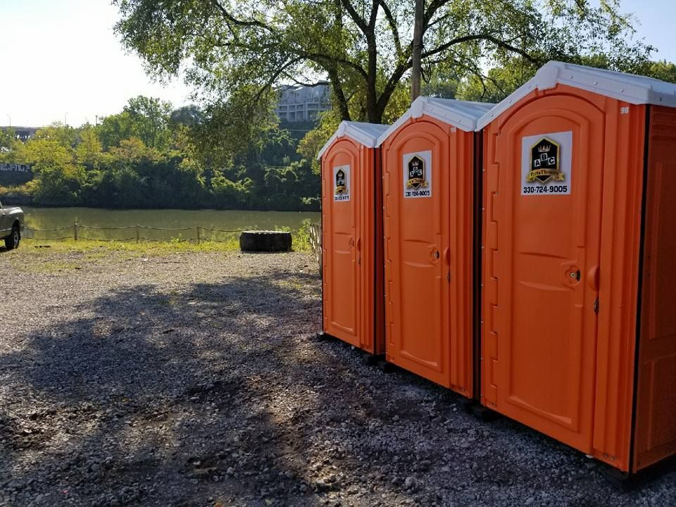 Three orange portable toilets are lined up in a gravel lot.