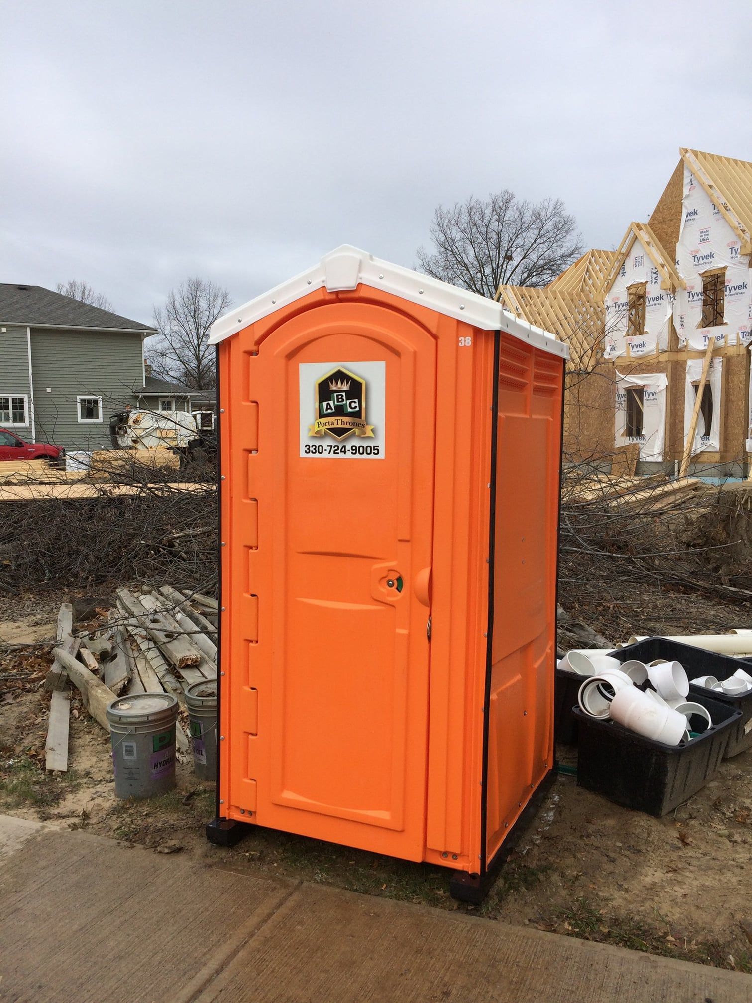 An orange portable toilet is sitting on the sidewalk in front of a construction site.