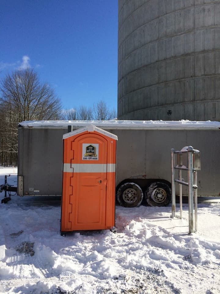 An orange portable toilet is parked in the snow next to a trailer.