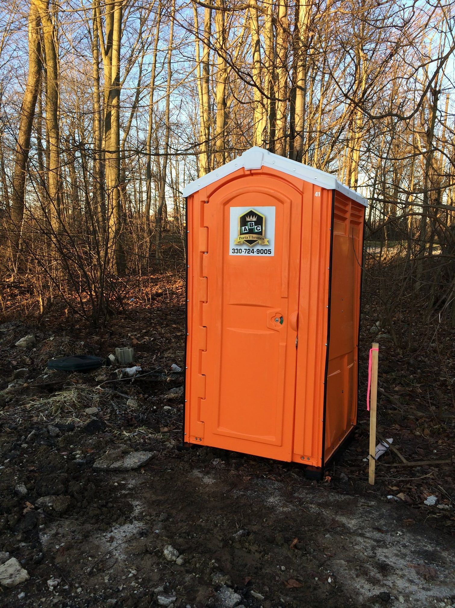 An orange portable toilet is sitting in the middle of a forest.