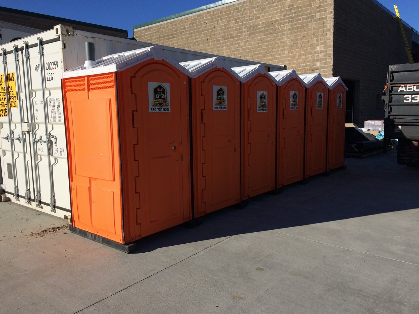 A row of orange portable toilets are lined up in a parking lot.
