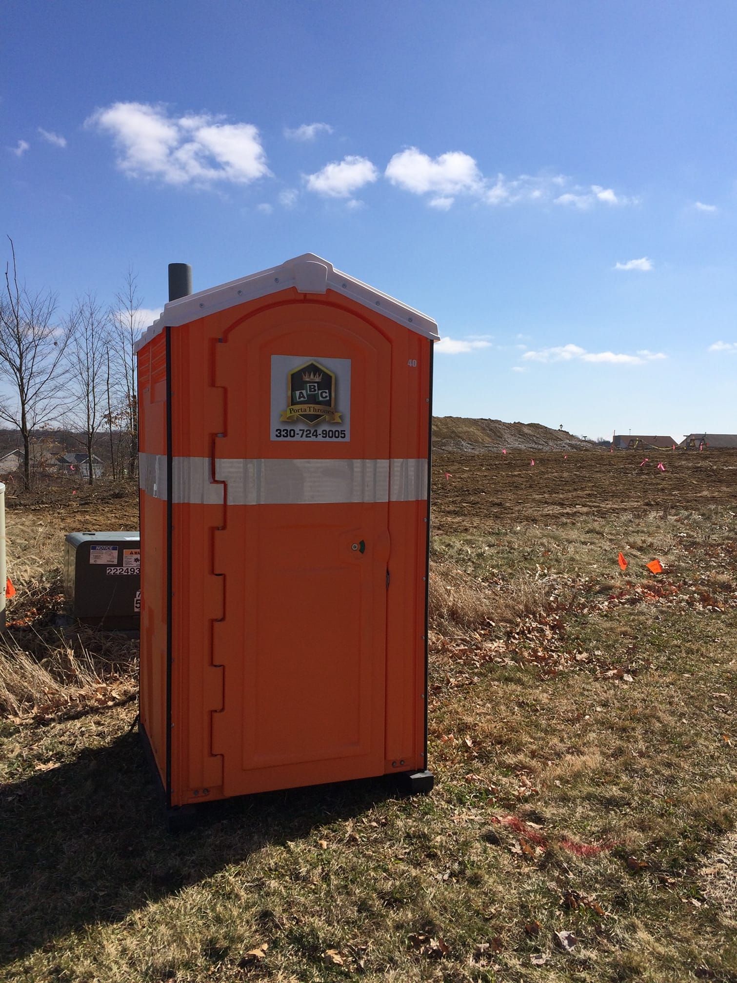 An orange portable toilet is sitting in the middle of a field.