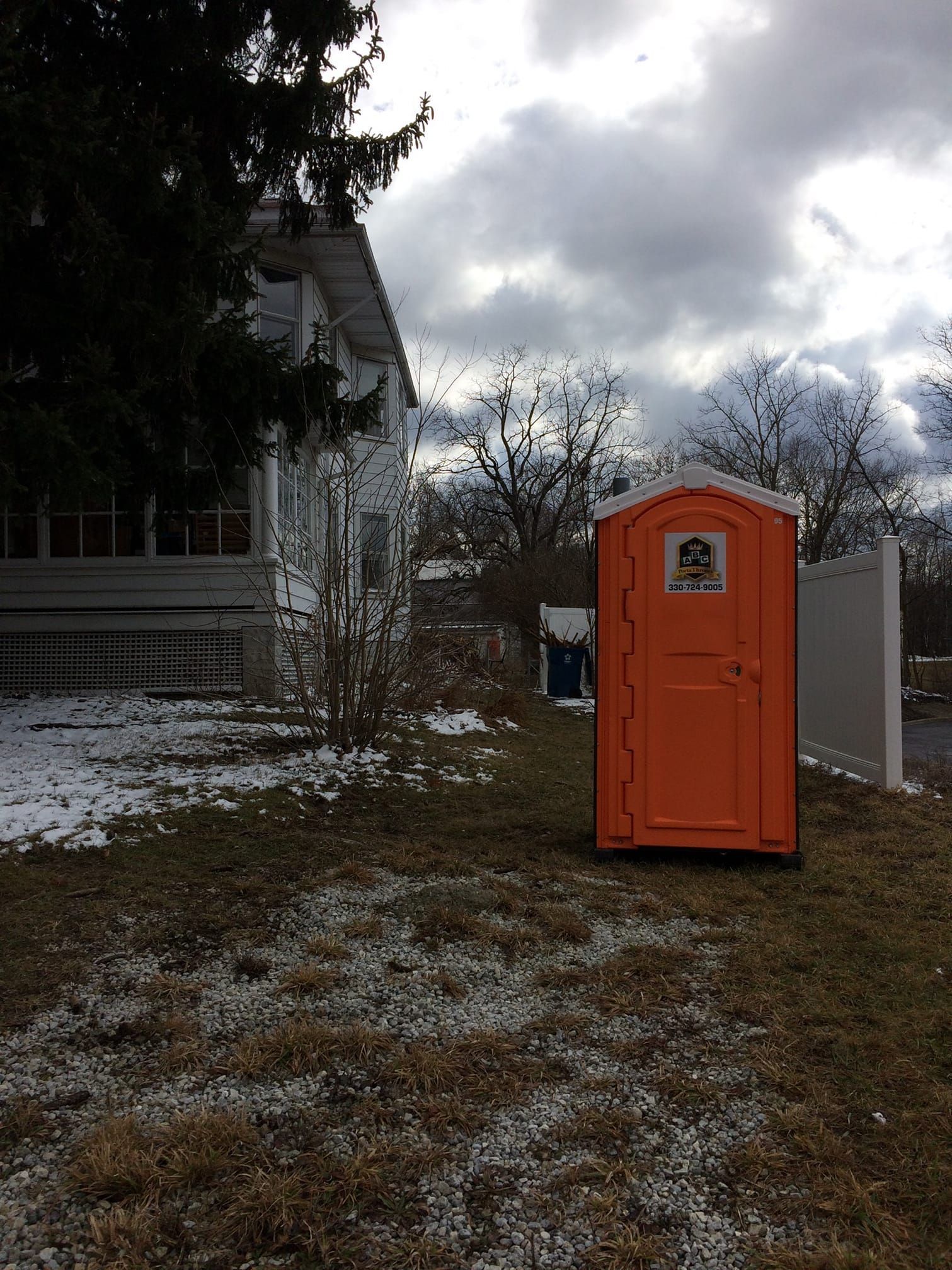 A small orange portable toilet is sitting in the grass in front of a house