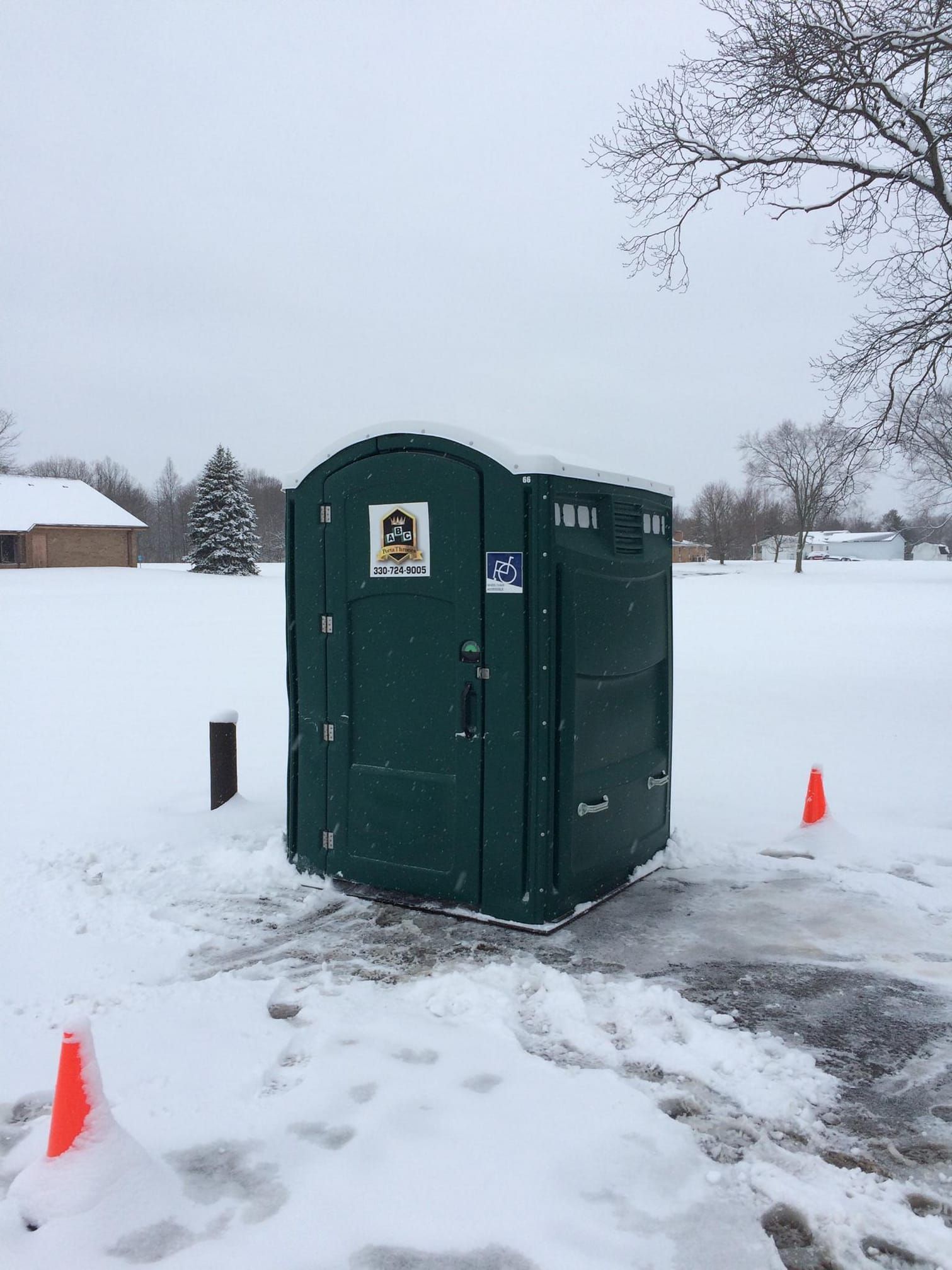 A green portable toilet is sitting in the middle of a snowy field.