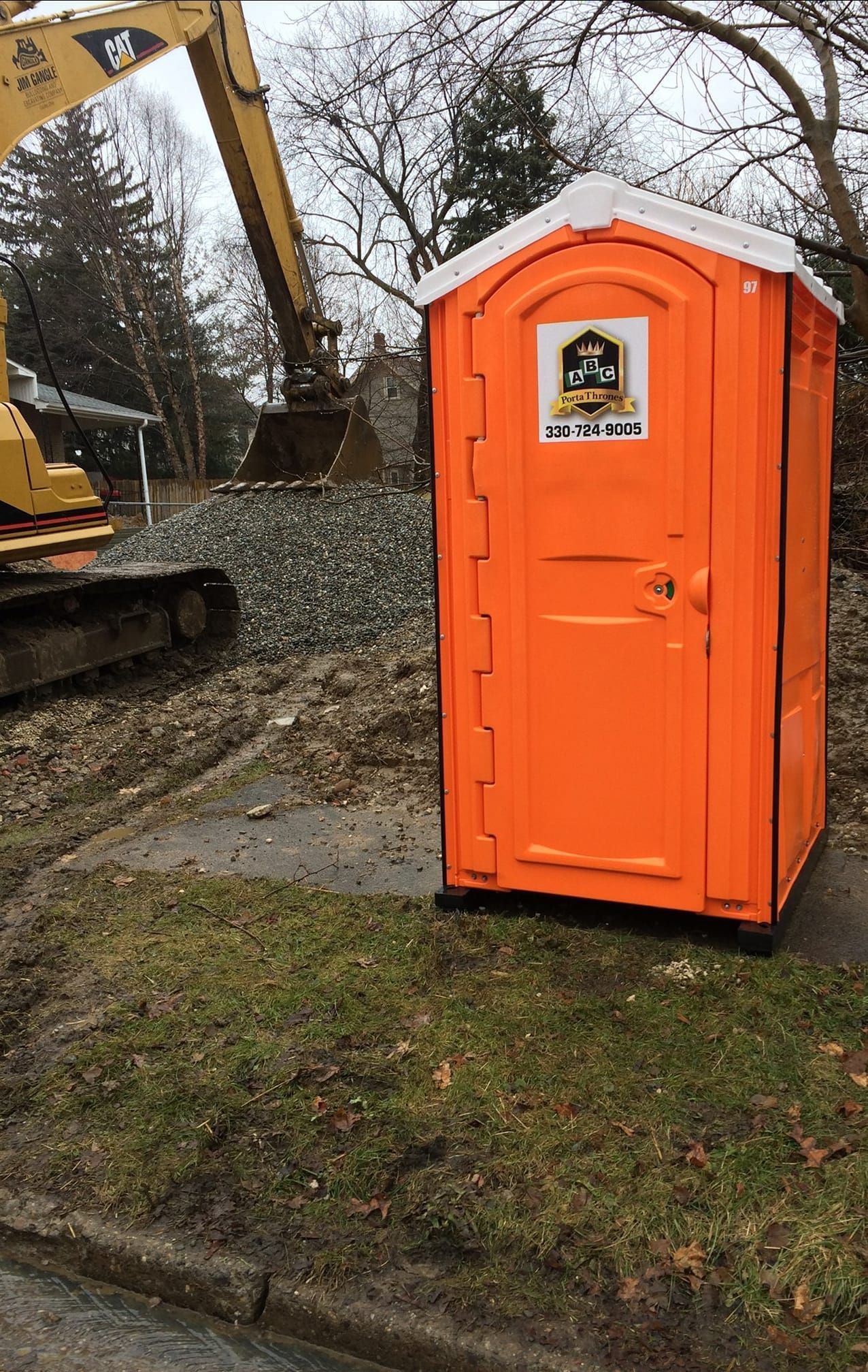 An orange portable toilet is sitting on the side of the road next to a bulldozer.