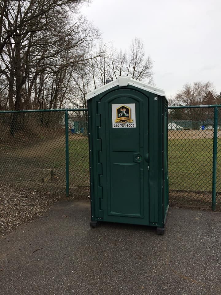 A green portable toilet is sitting next to a chain link fence.