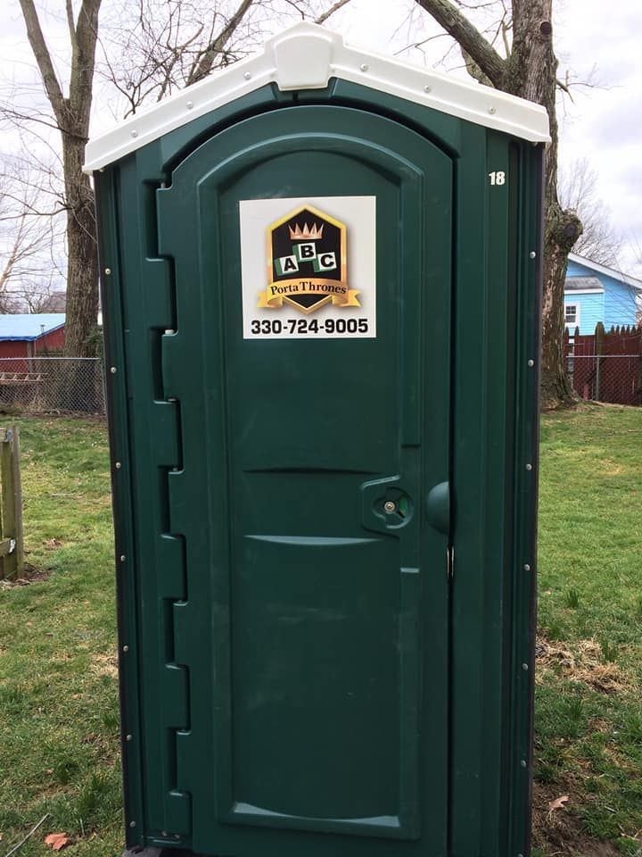 A green portable toilet is sitting on top of a lush green field.