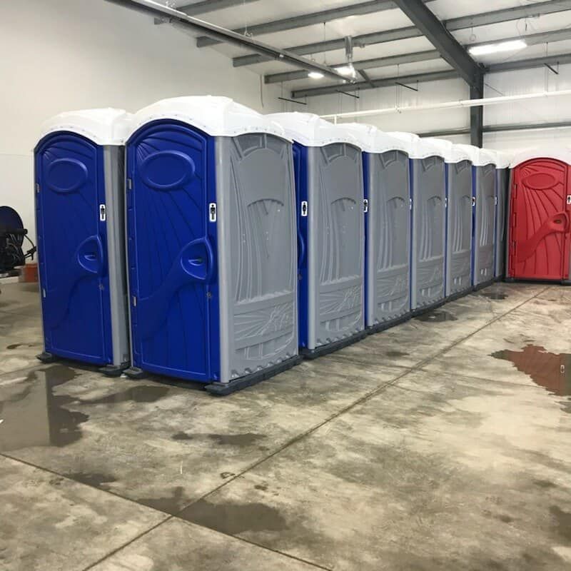 A row of portable toilets are lined up in a warehouse.
