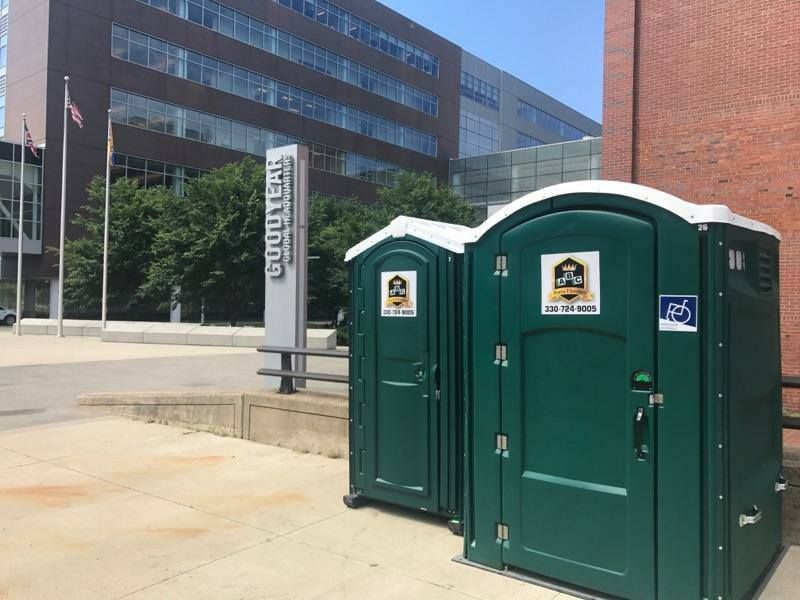 Two green portable toilets are sitting on the sidewalk in front of a building.