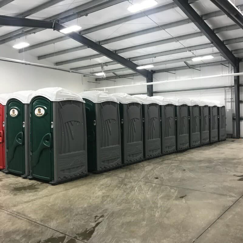 A row of portable toilets are lined up in a warehouse.