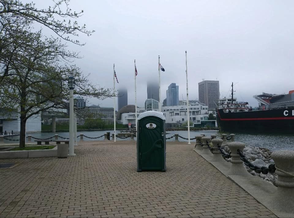 A small green portable toilet sits in front of a large ship that says cle