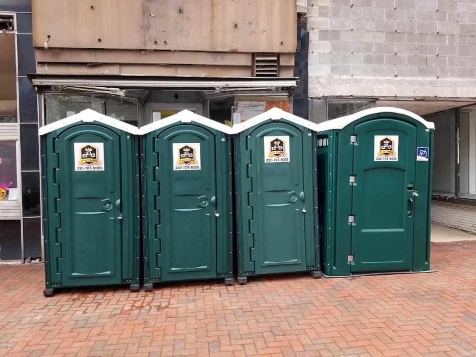 A row of green portable toilets are lined up on a brick sidewalk.