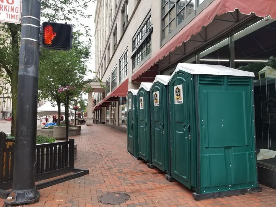A row of green portable toilets on a sidewalk in front of a building