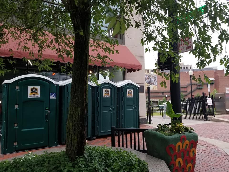 A row of green portable toilets are parked in front of a building.