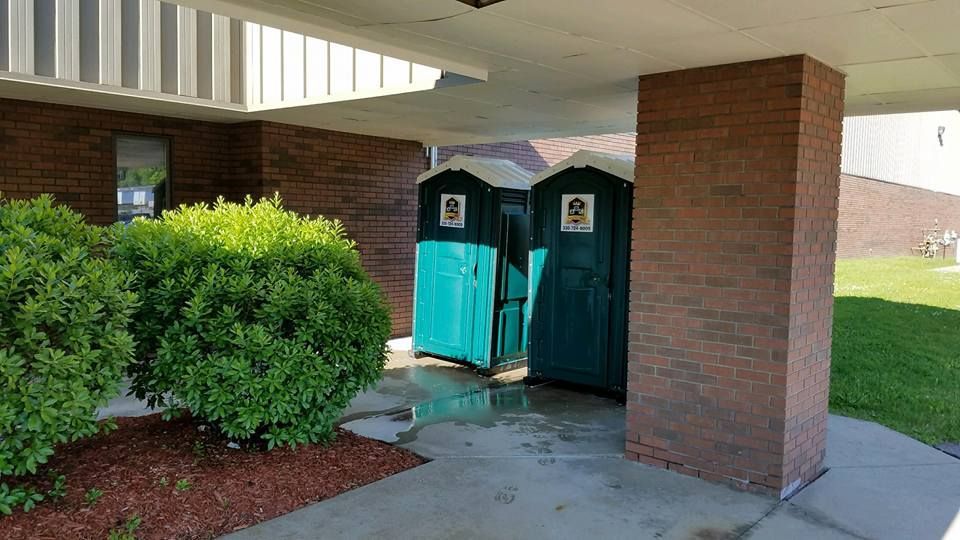 Two portable toilets are sitting under a brick building.