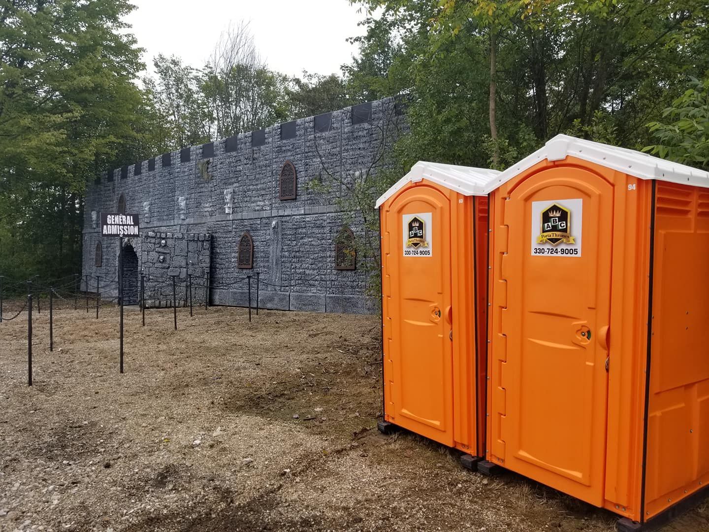 Two orange portable toilets are sitting next to each other in front of a castle.