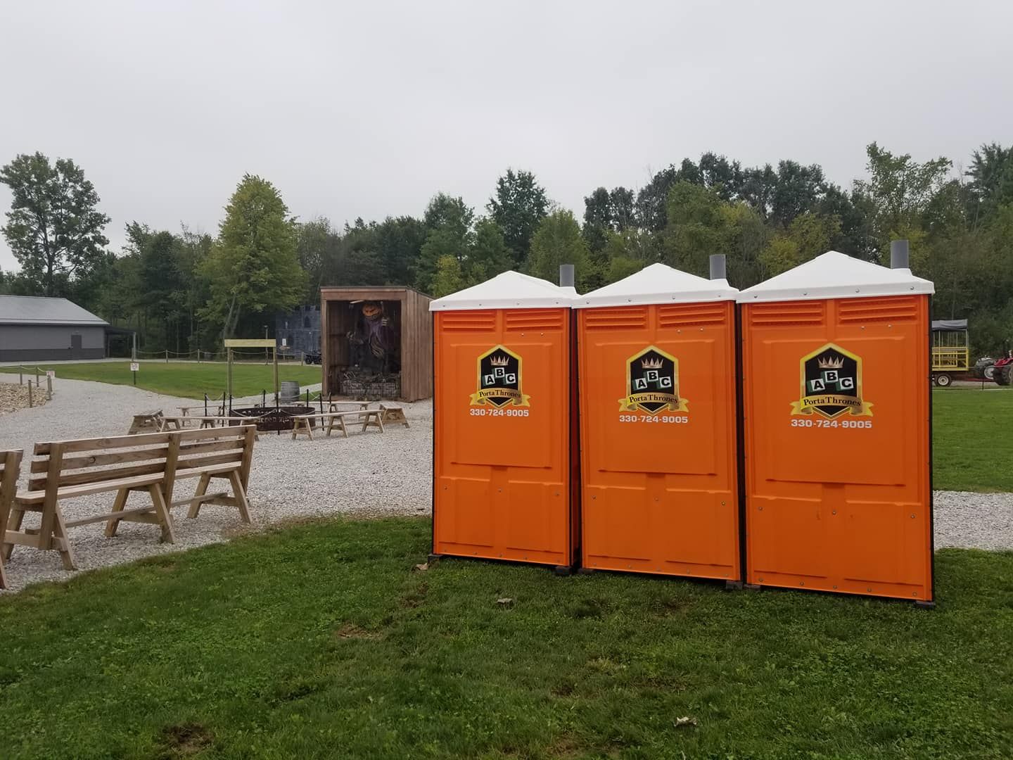 Three orange portable toilets are lined up in a grassy field.