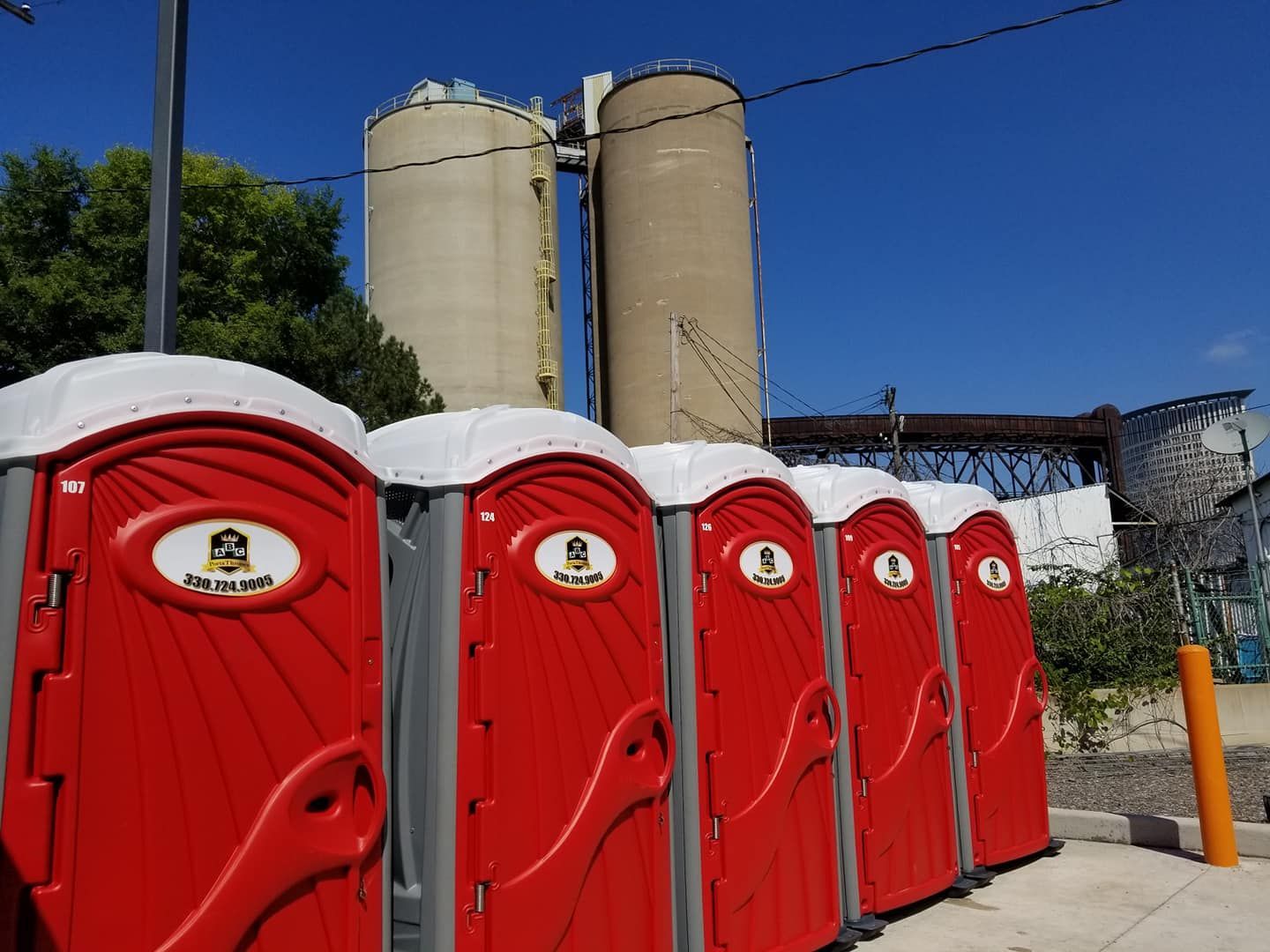 A row of red portable toilets are lined up in front of a factory.