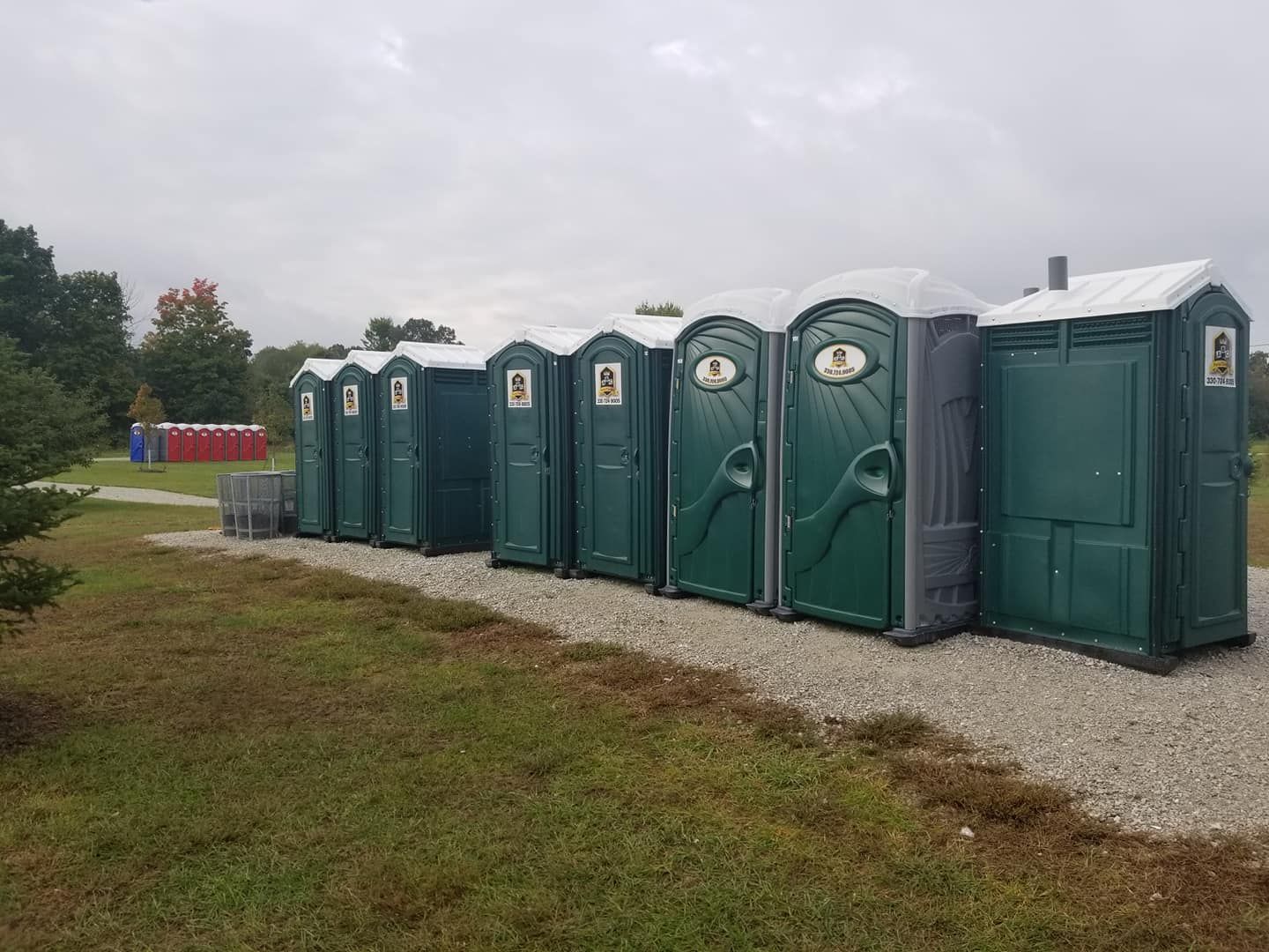 A row of green portable toilets are lined up in a grassy field.