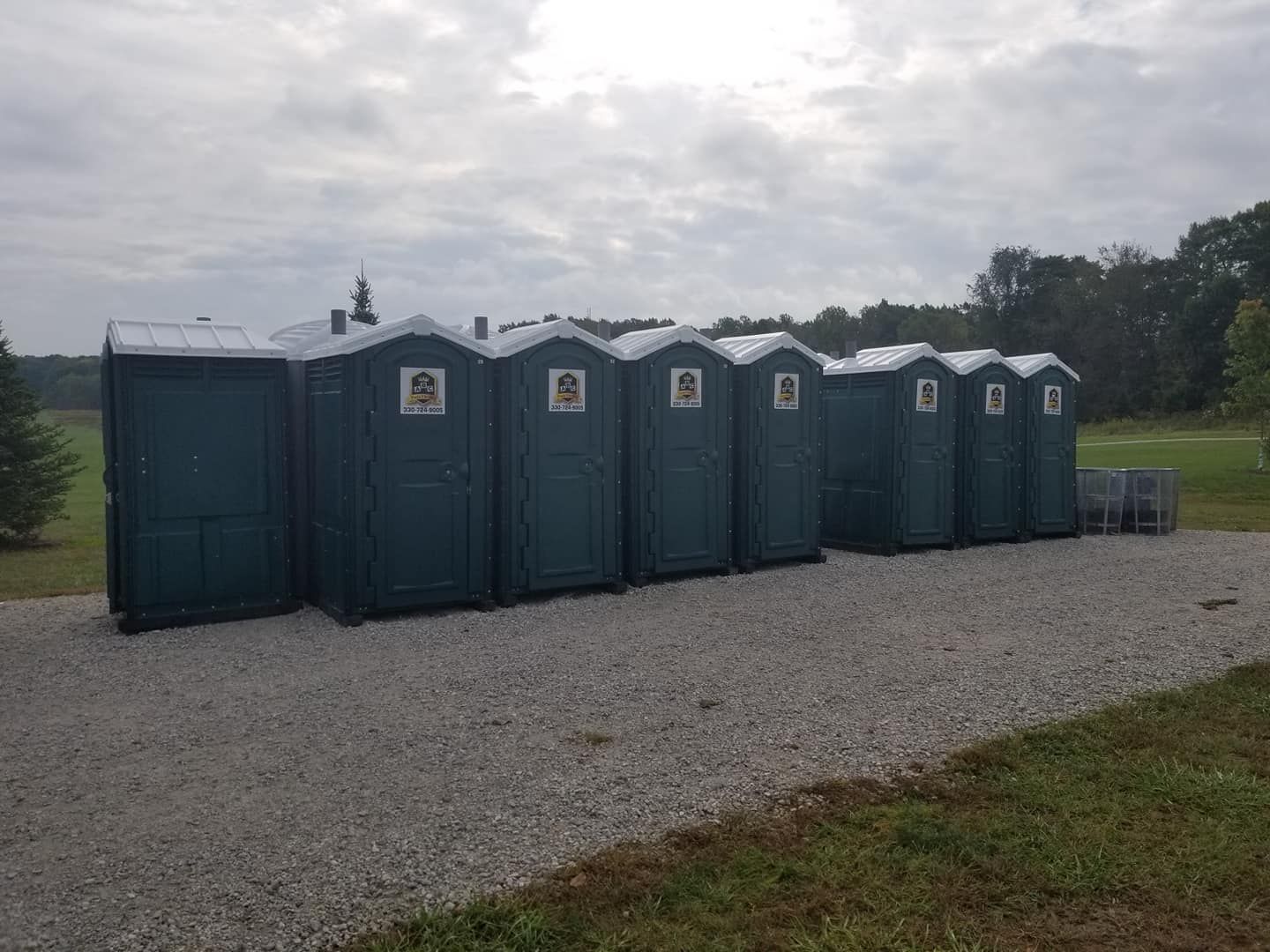 A row of portable toilets are lined up in a gravel driveway.