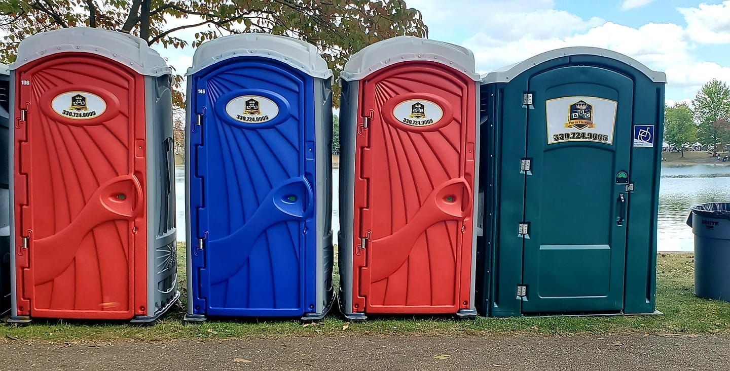 A row of red , blue , and green portable toilets are lined up next to each other.
