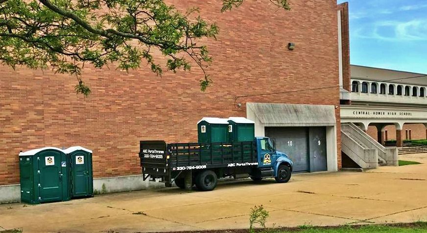 A truck and two portable toilets are parked in front of a brick building.