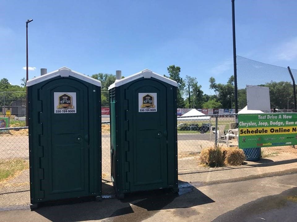 Two green portable toilets are sitting next to each other in a parking lot.