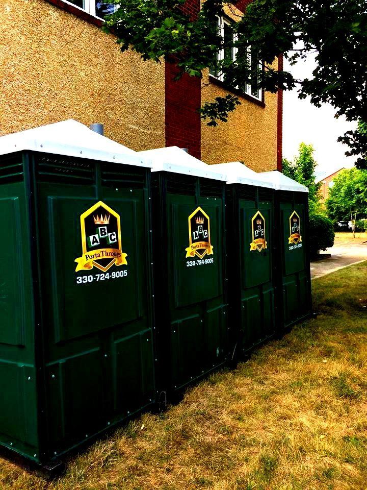 A row of green portable toilets are lined up in front of a building.