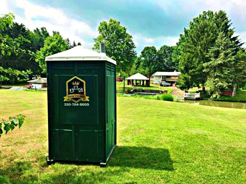 A green portable toilet is sitting in the middle of a grassy field.