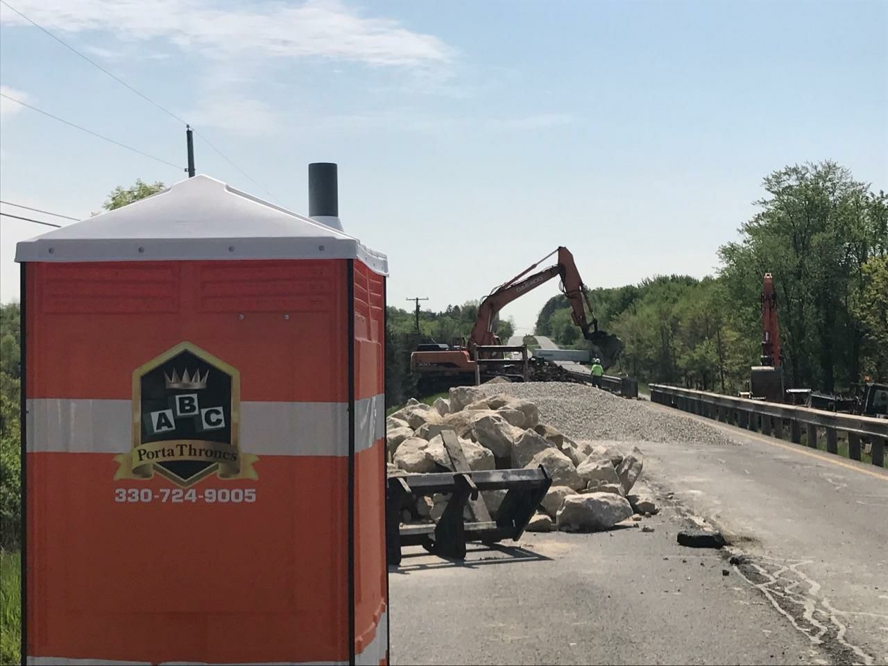 A portable toilet is sitting on the side of a road next to a construction site.