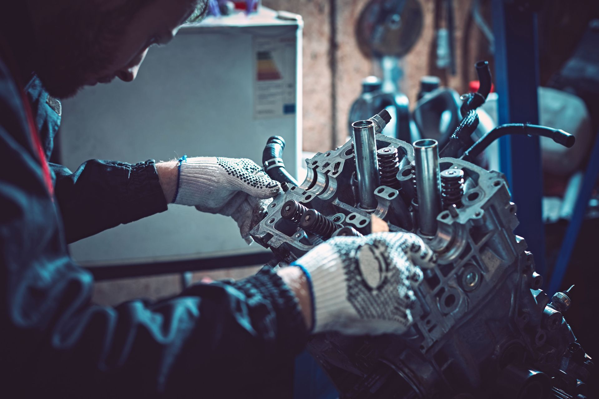 Mechanic in a garage working on a car engine, wearing gloves, focused.