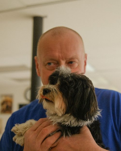 A man in a blue shirt is holding a small dog