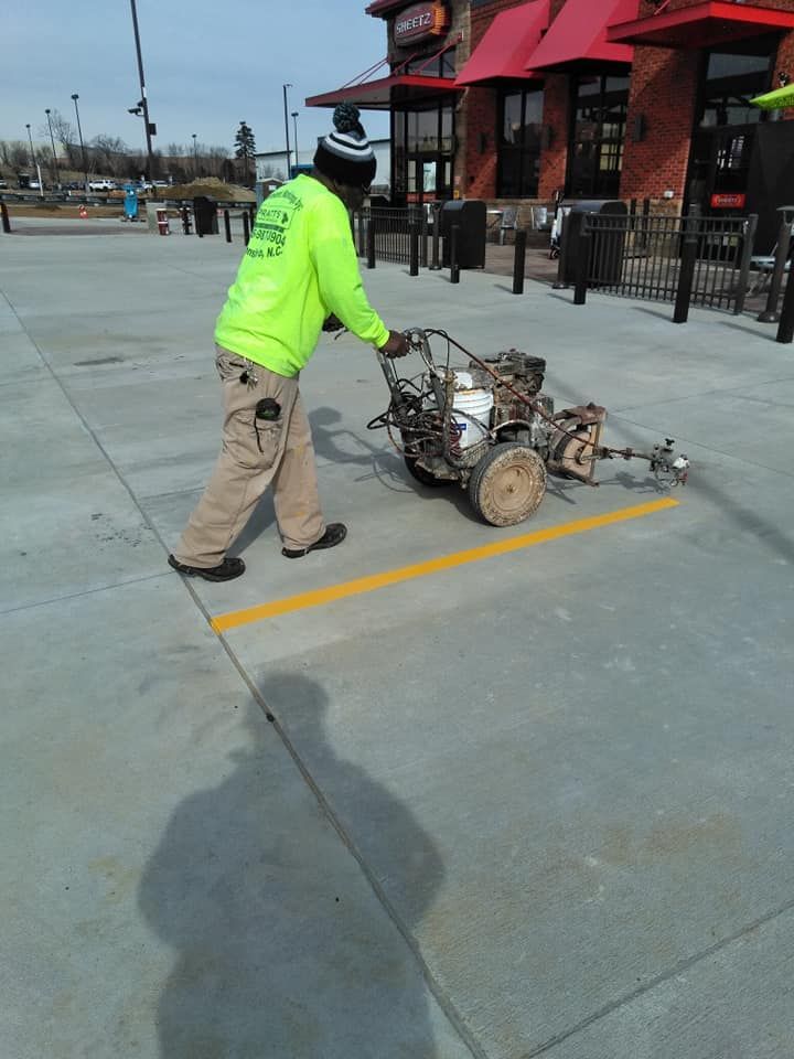 A man in a neon green shirt is painting a yellow line on the sidewalk