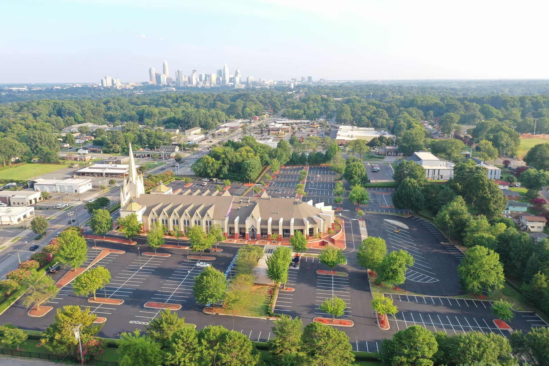 An aerial view of a church and parking lot with a city in the background.