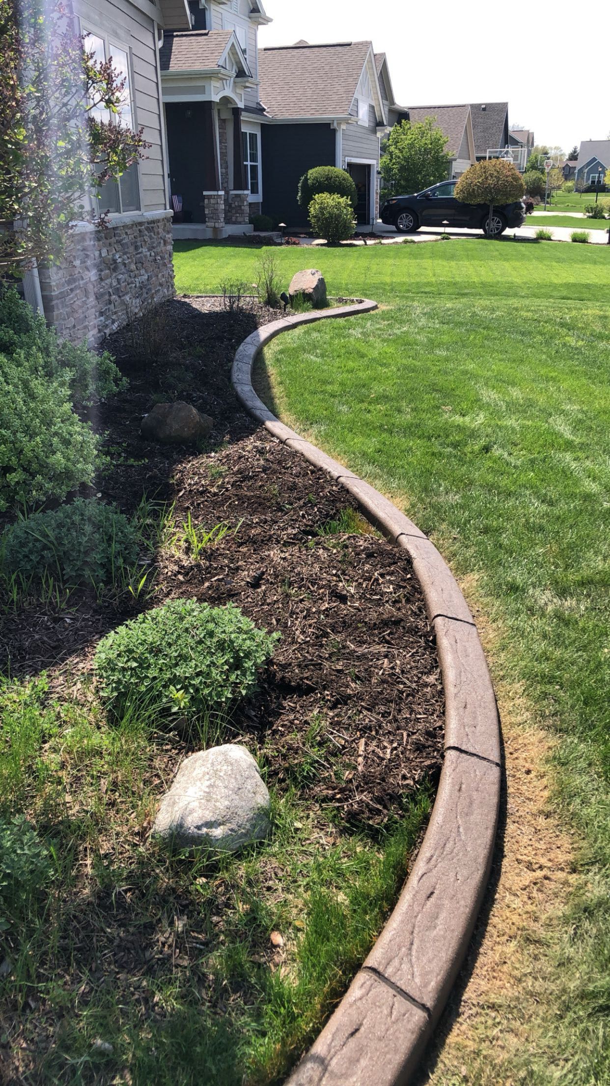 A lawn with a concrete curb and a rock in the middle of it.