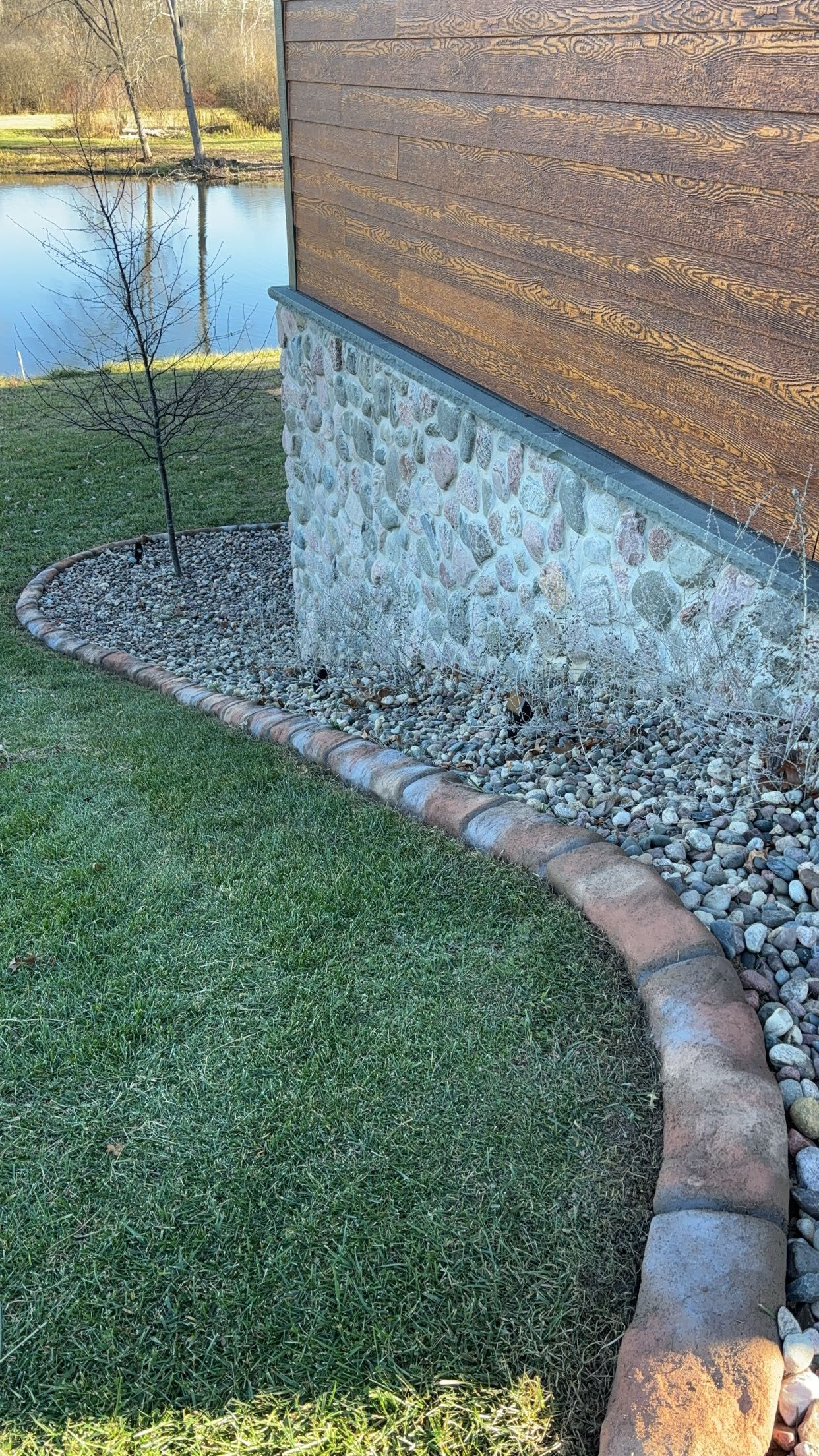 A stone walkway leading to a house with a pond in the background.