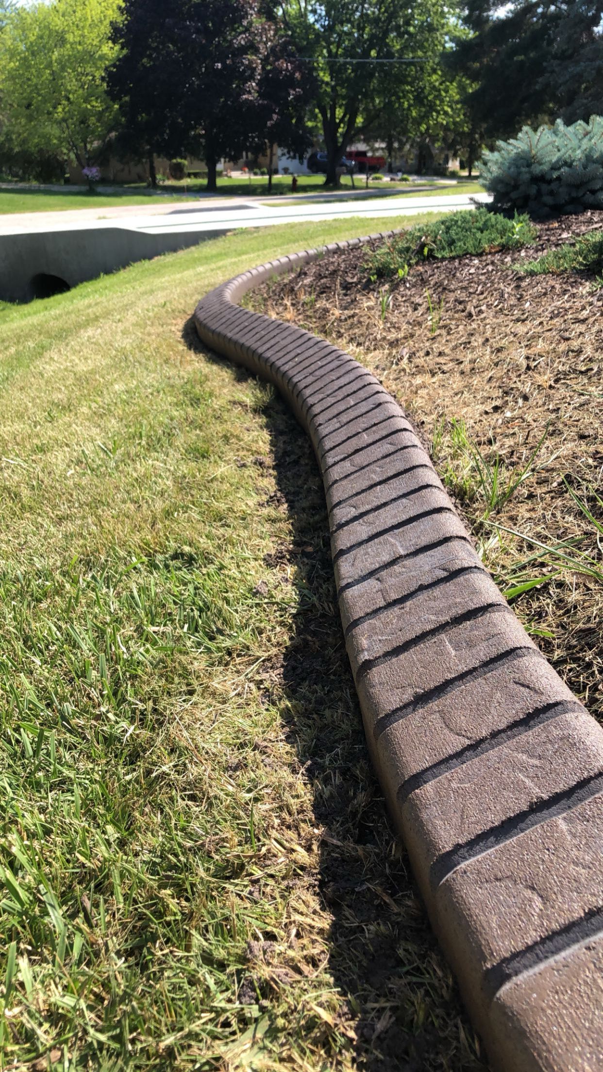 A brick curb is surrounded by grass and trees in a park.