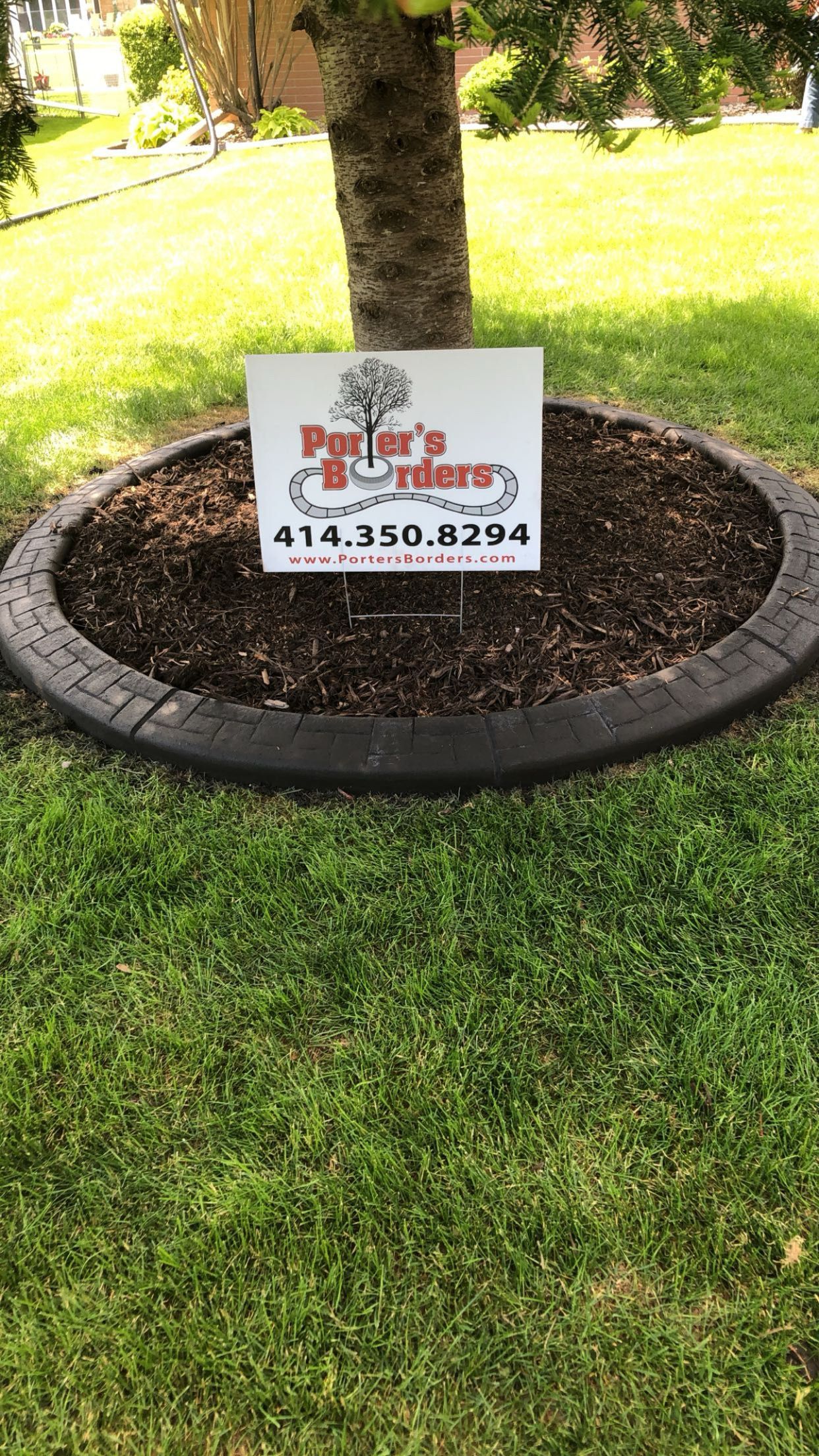 A sign is sitting in the grass next to a tree.
