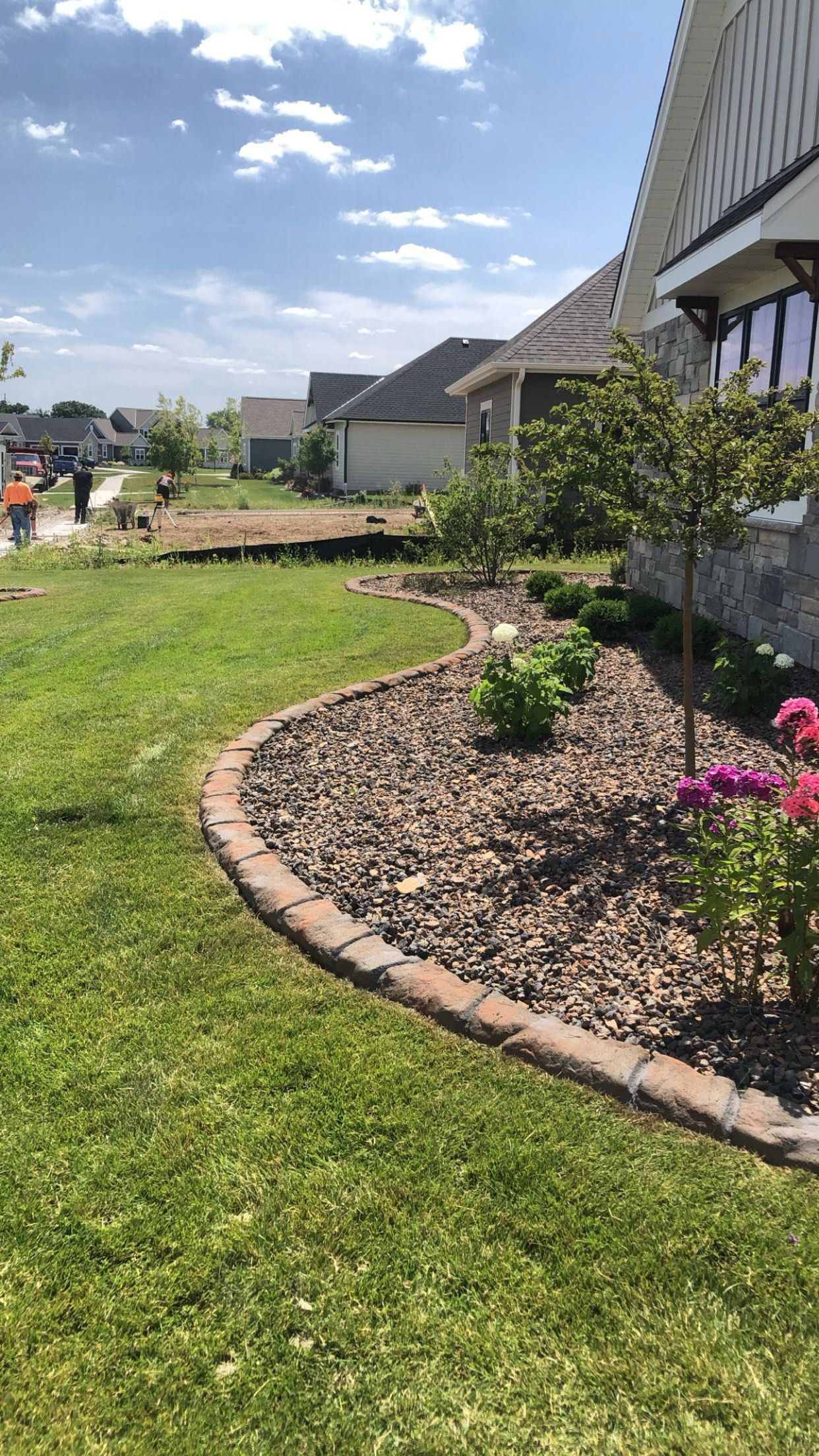 A lush green lawn with a brick border and flowers in front of a house.