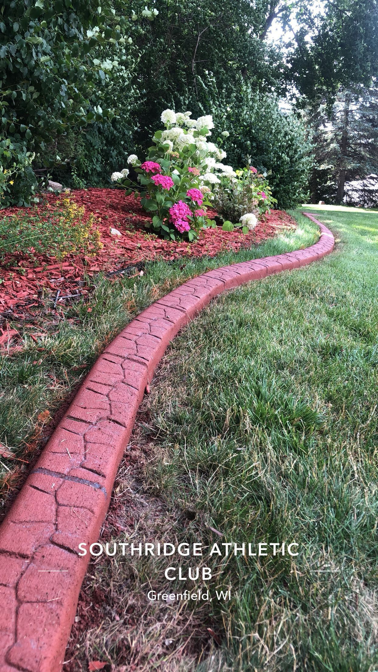 A red brick curb is in the middle of a lush green lawn.