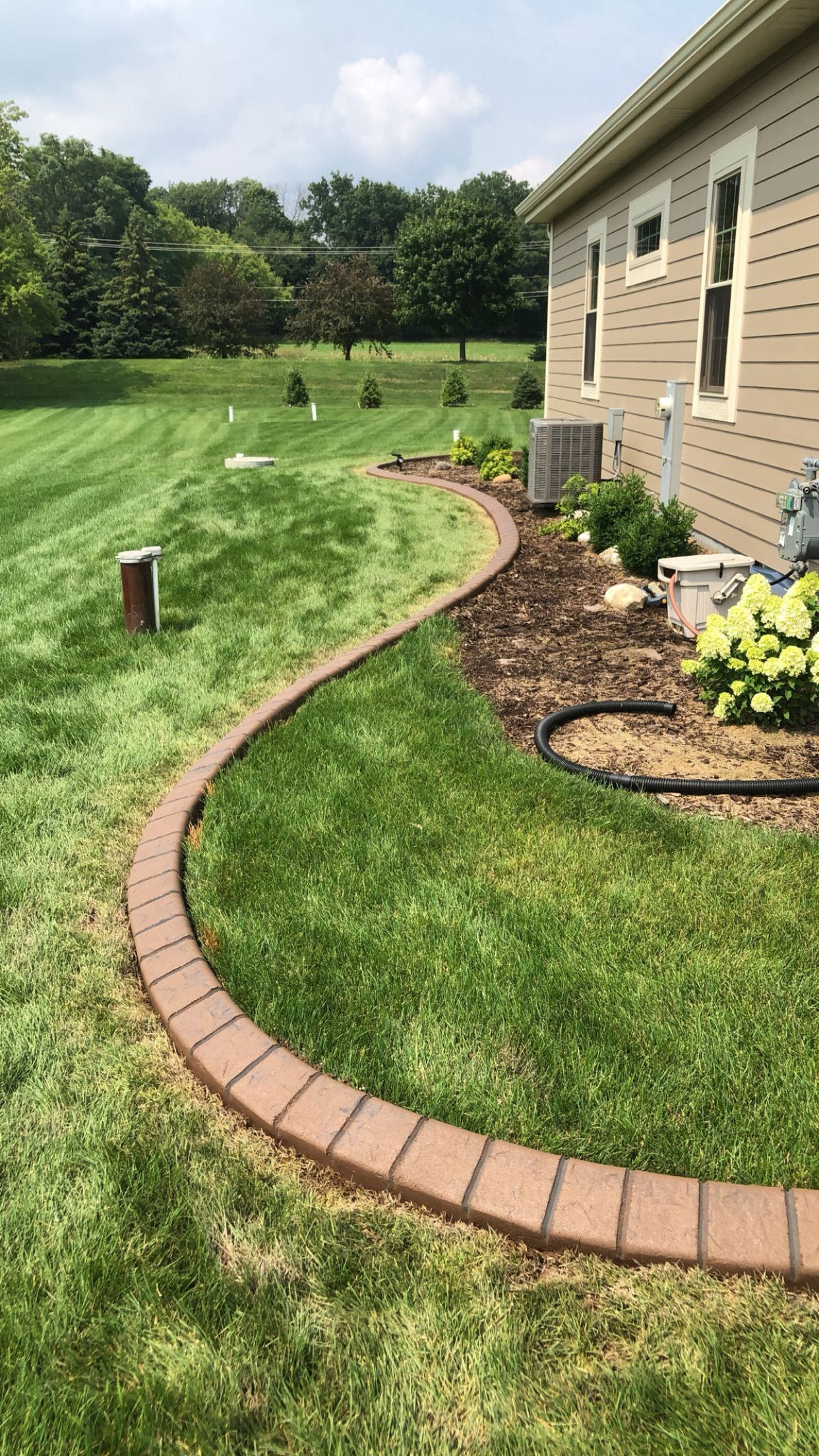 A brick walkway going through a lush green lawn next to a house.