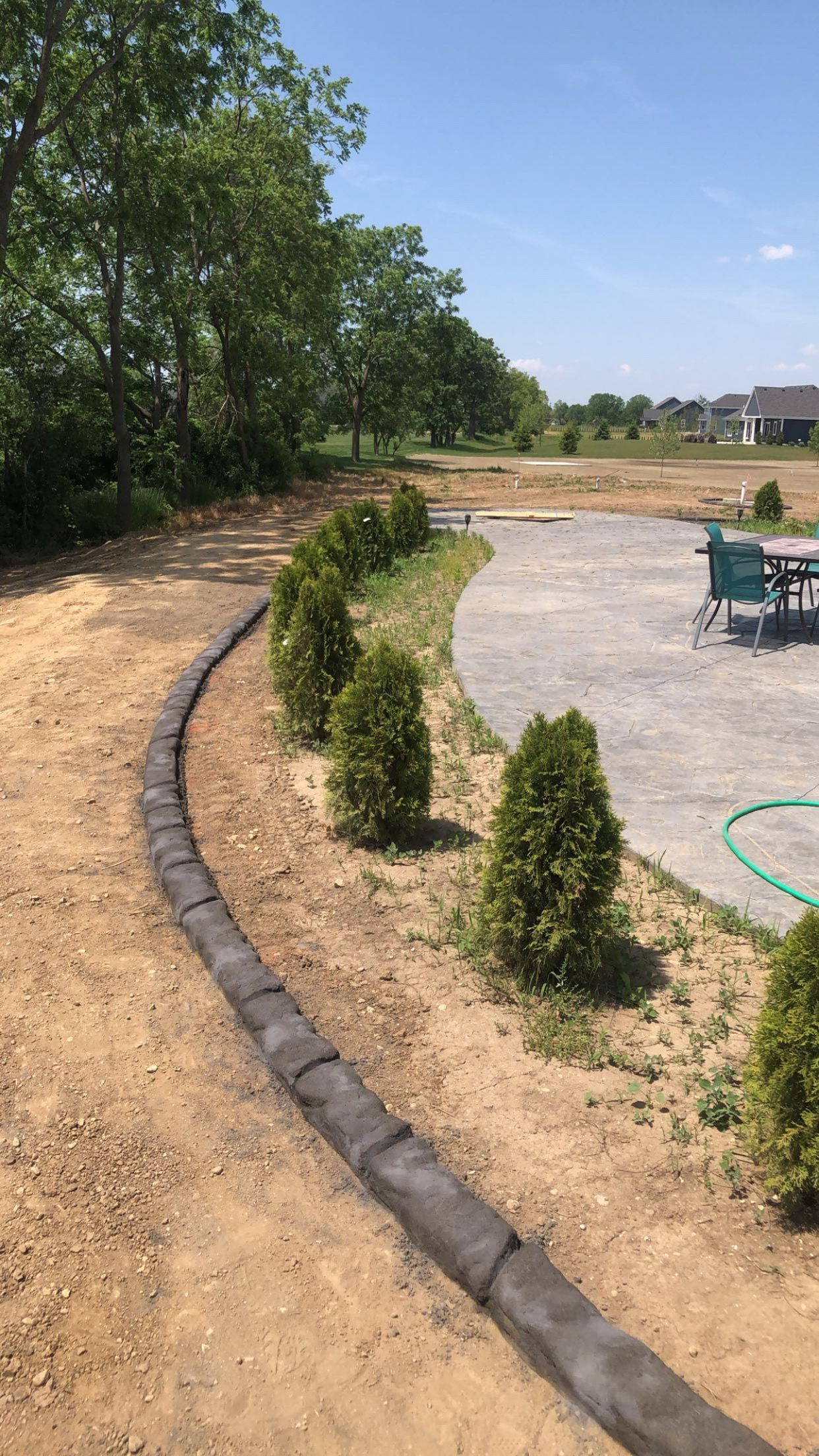 A concrete curb in a backyard with trees and a patio in the background.