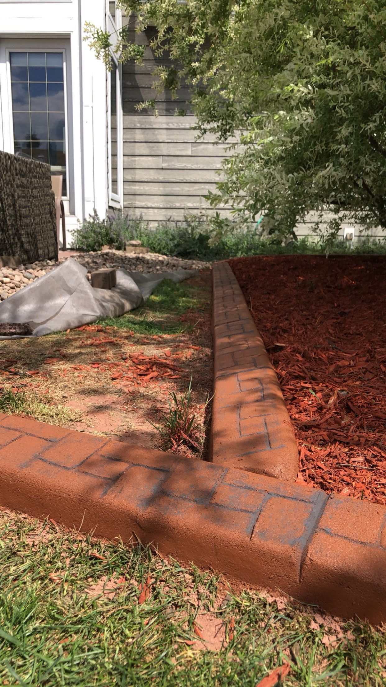 A brick curb in a yard next to a pile of mulch.