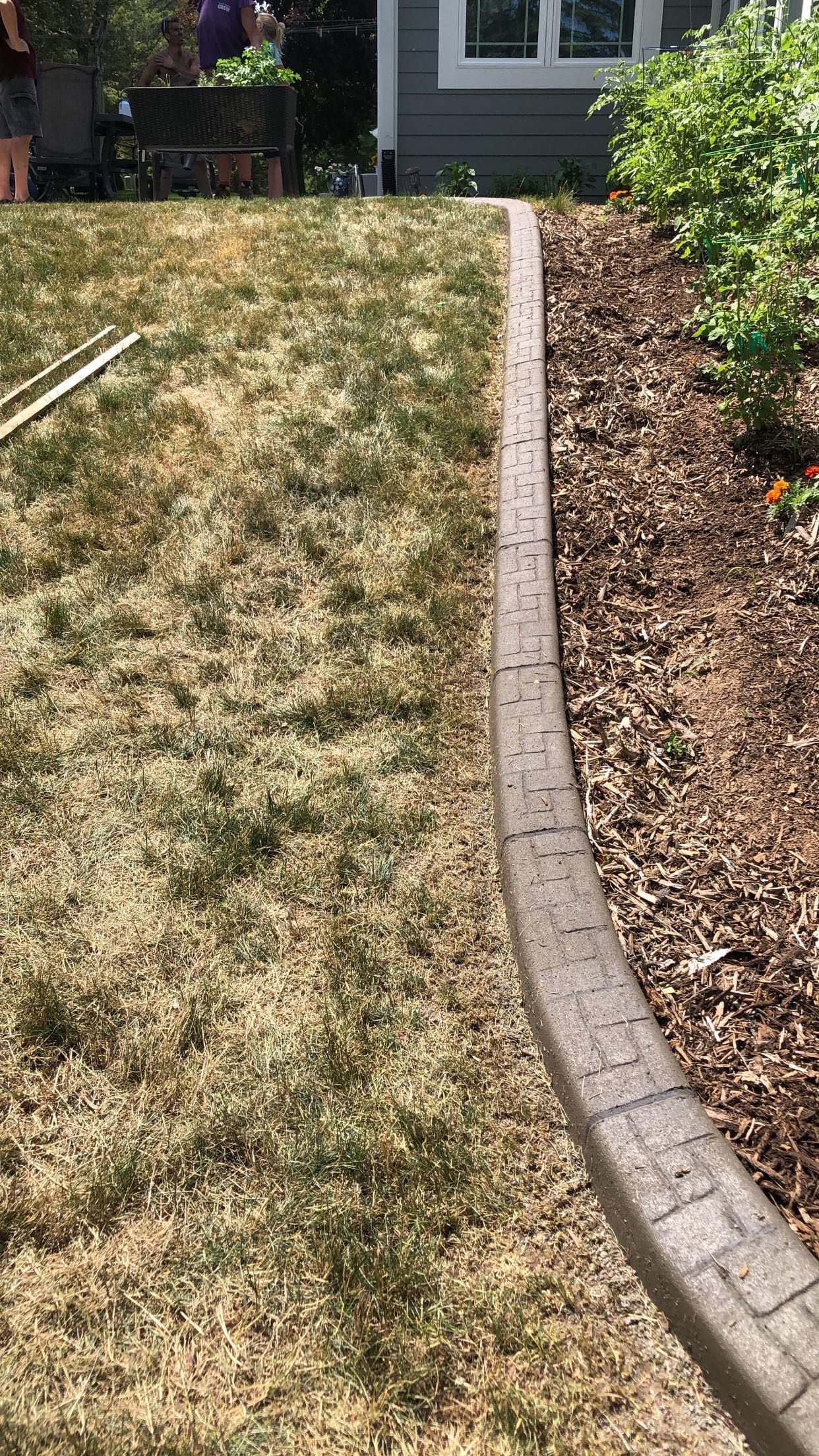 A person is mowing a lawn next to a brick curb.