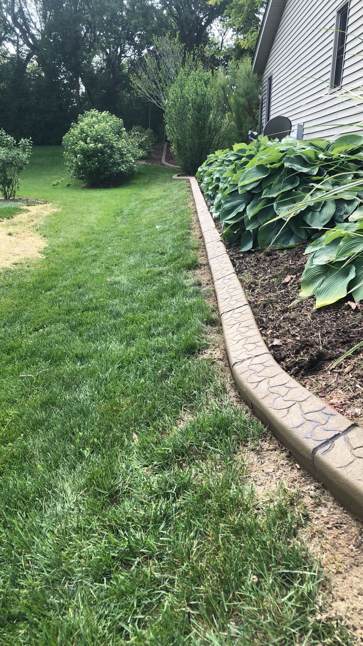 A lawn with a concrete curb and a house in the background.