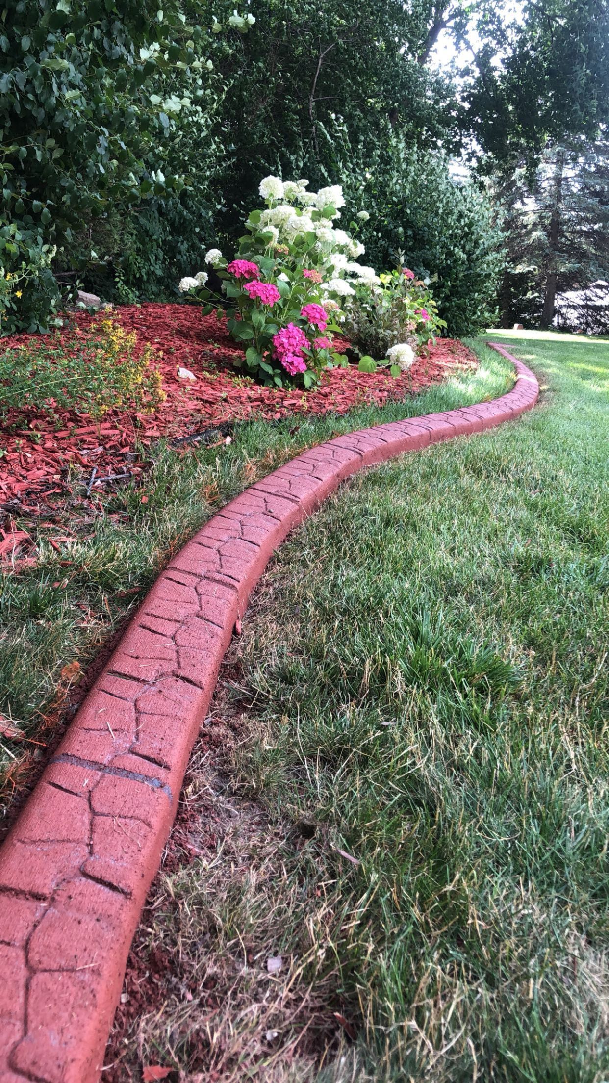 A red concrete curb in the middle of a lush green lawn.