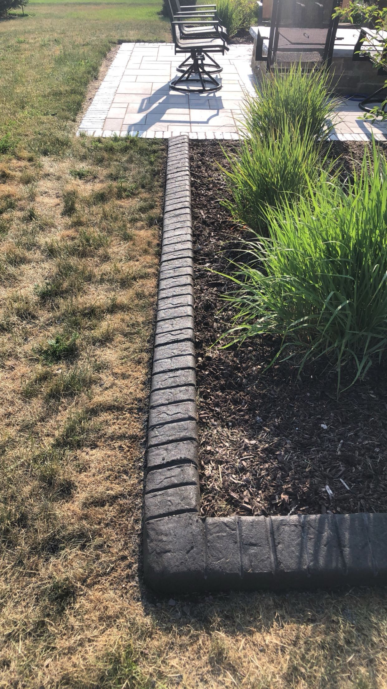 A lawn with a brick border and a patio in the background.