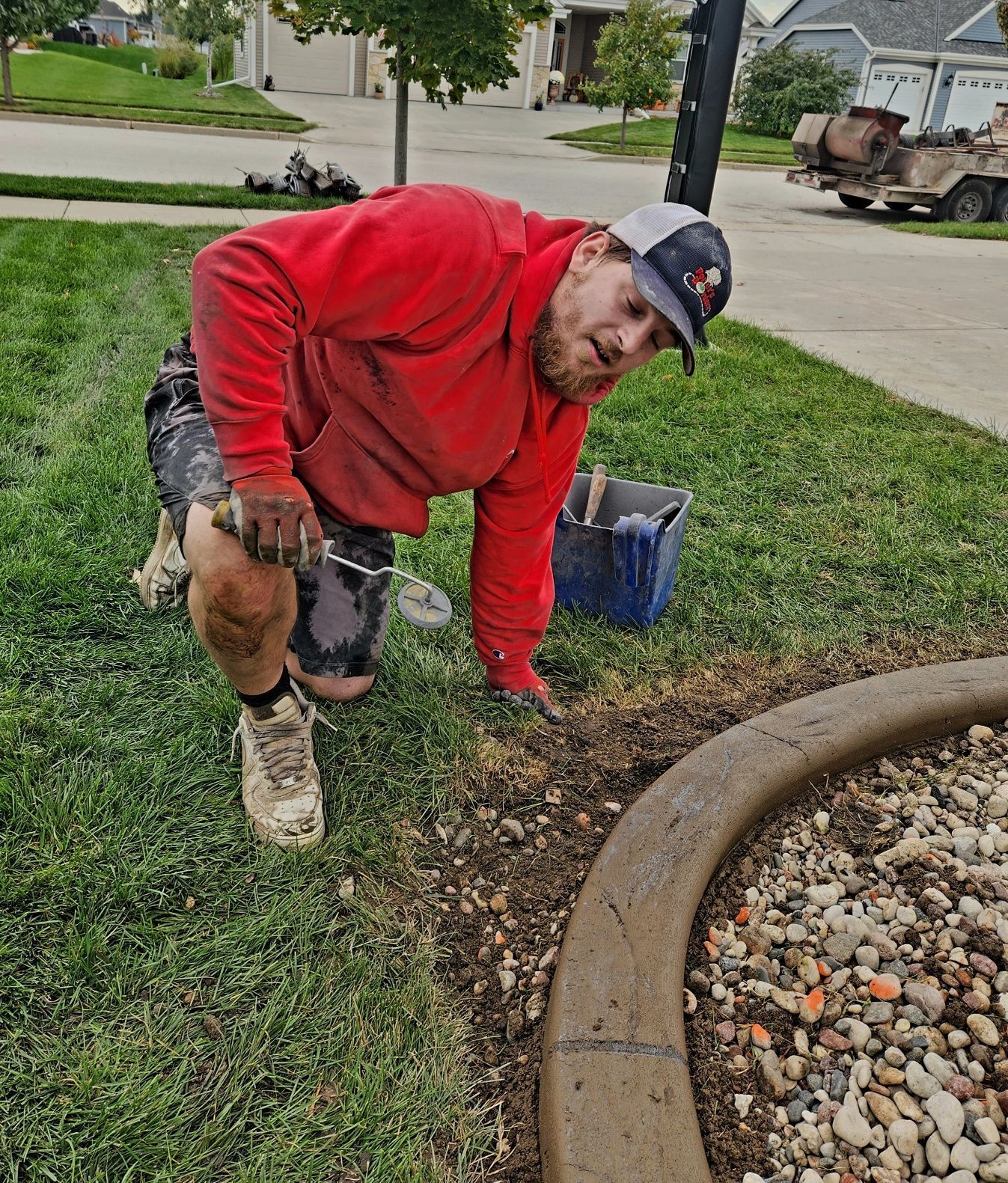 A man in a red shirt is kneeling down in the grass.