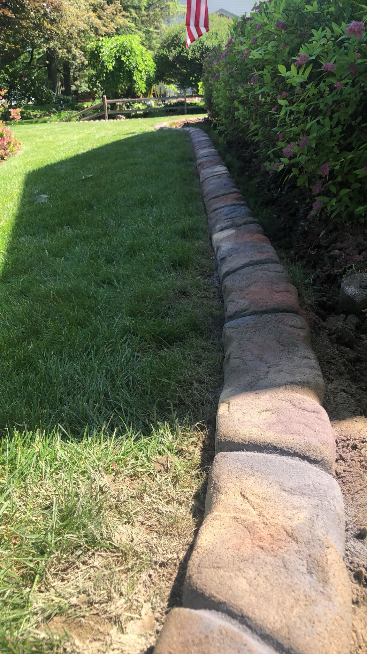 A stone walkway leading to a lush green lawn with a flag in the background.